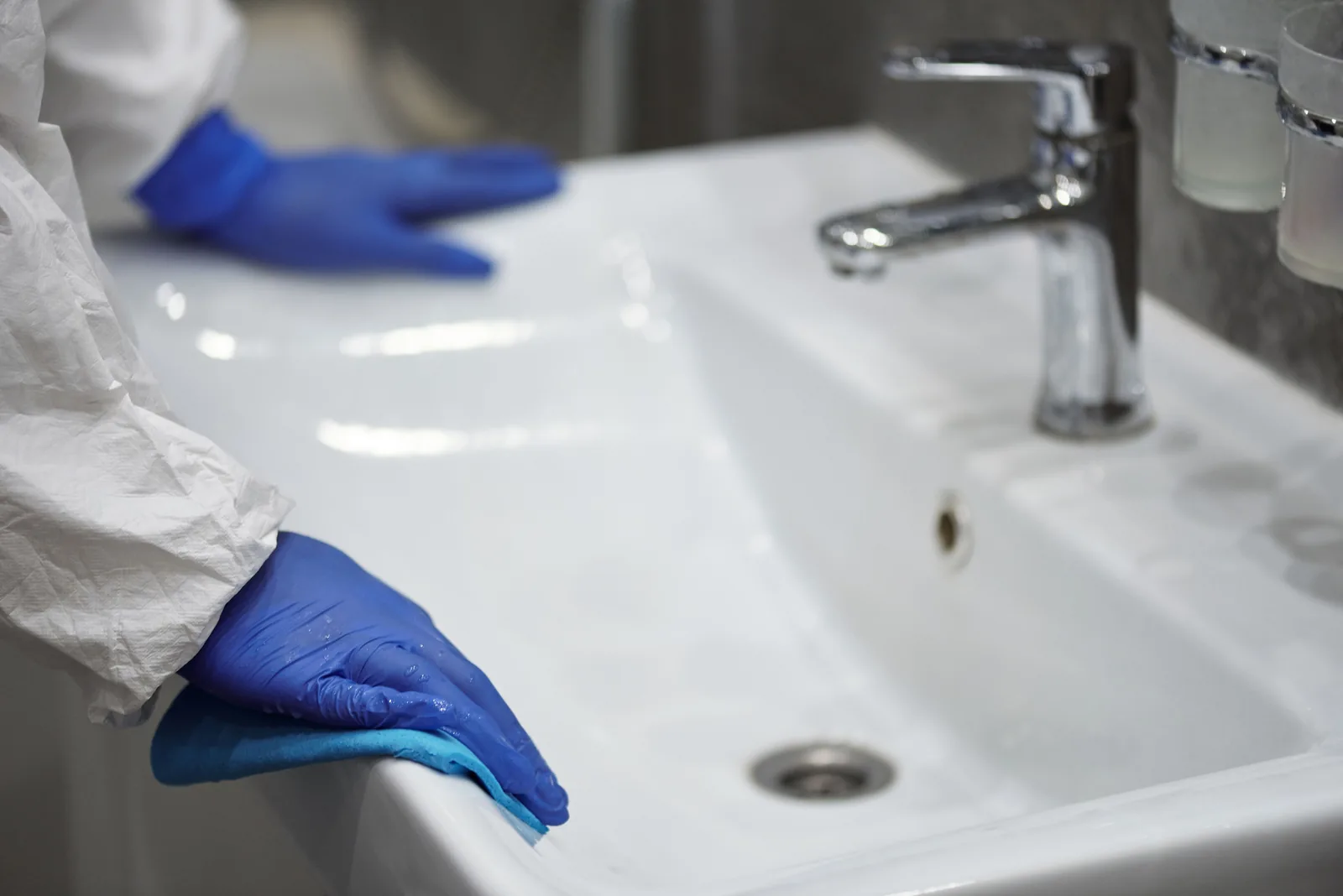 Gloved hands wiping a restroom sink